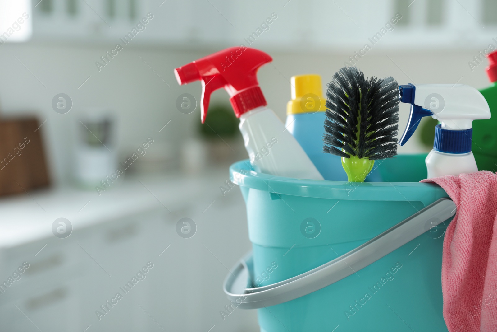 Photo of Plastic bucket with different cleaning supplies in kitchen, closeup. Space for text