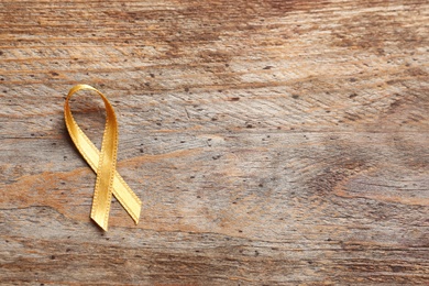 Gold ribbon on wooden background, top view. Cancer awareness