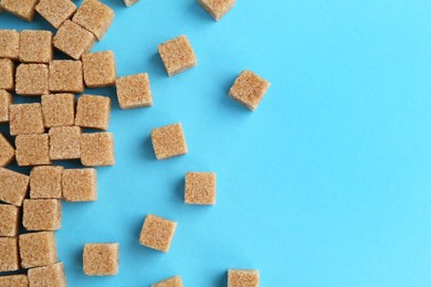 Photo of Brown sugar cubes on light blue background, top view. Space for text