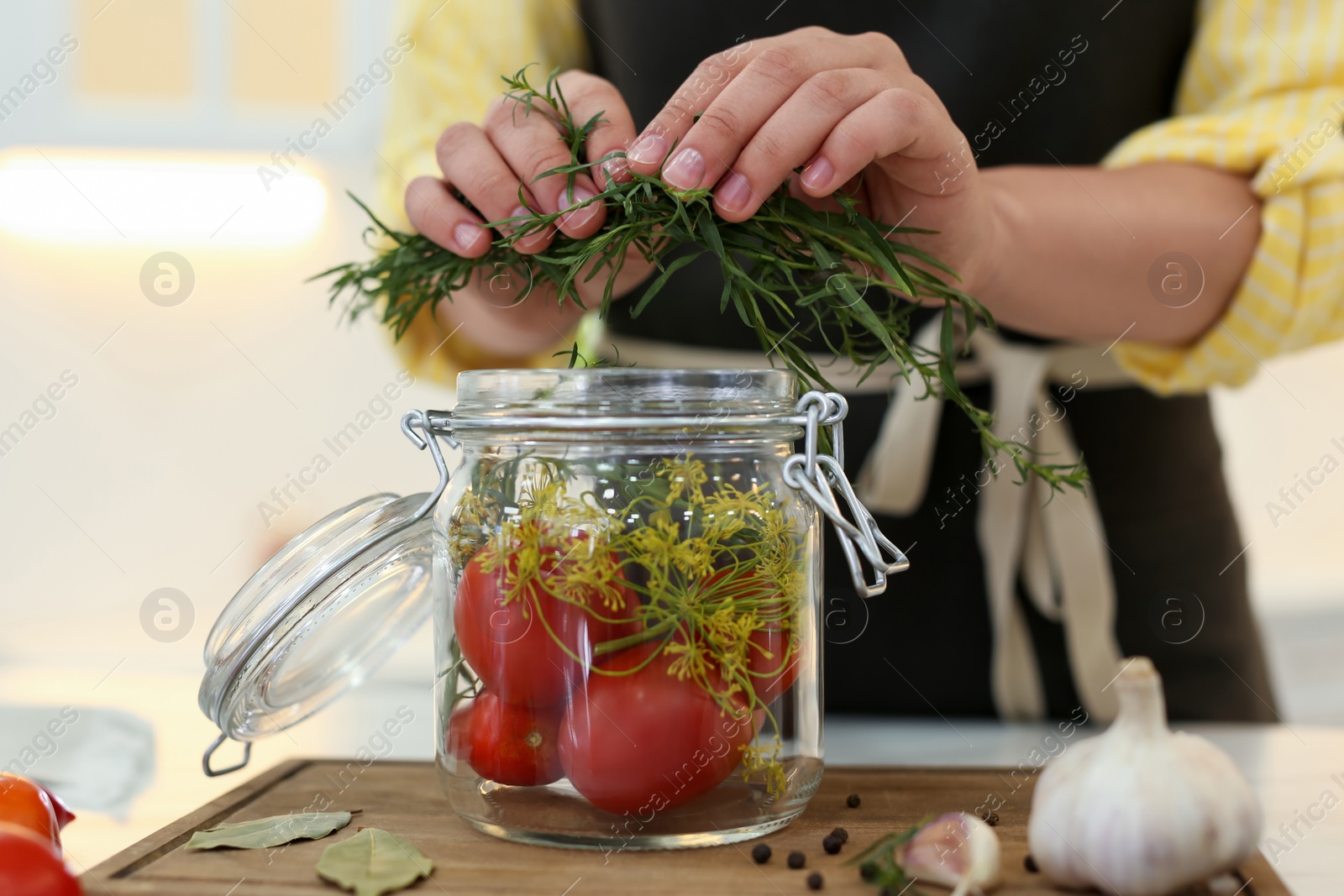 Photo of Woman putting rosemary into pickling jar at kitchen table, closeup