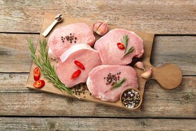 Photo of Pieces of raw pork meat and spices on wooden table, top view