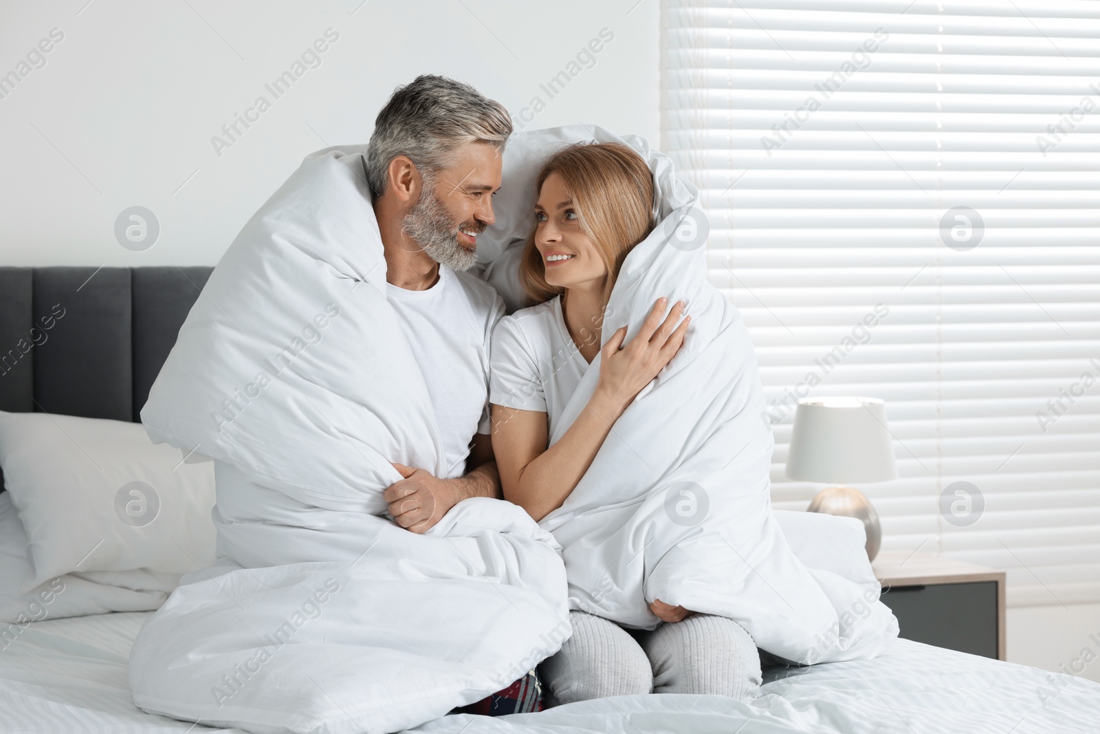 Photo of Lovely mature couple wrapped in blanket on bed at home