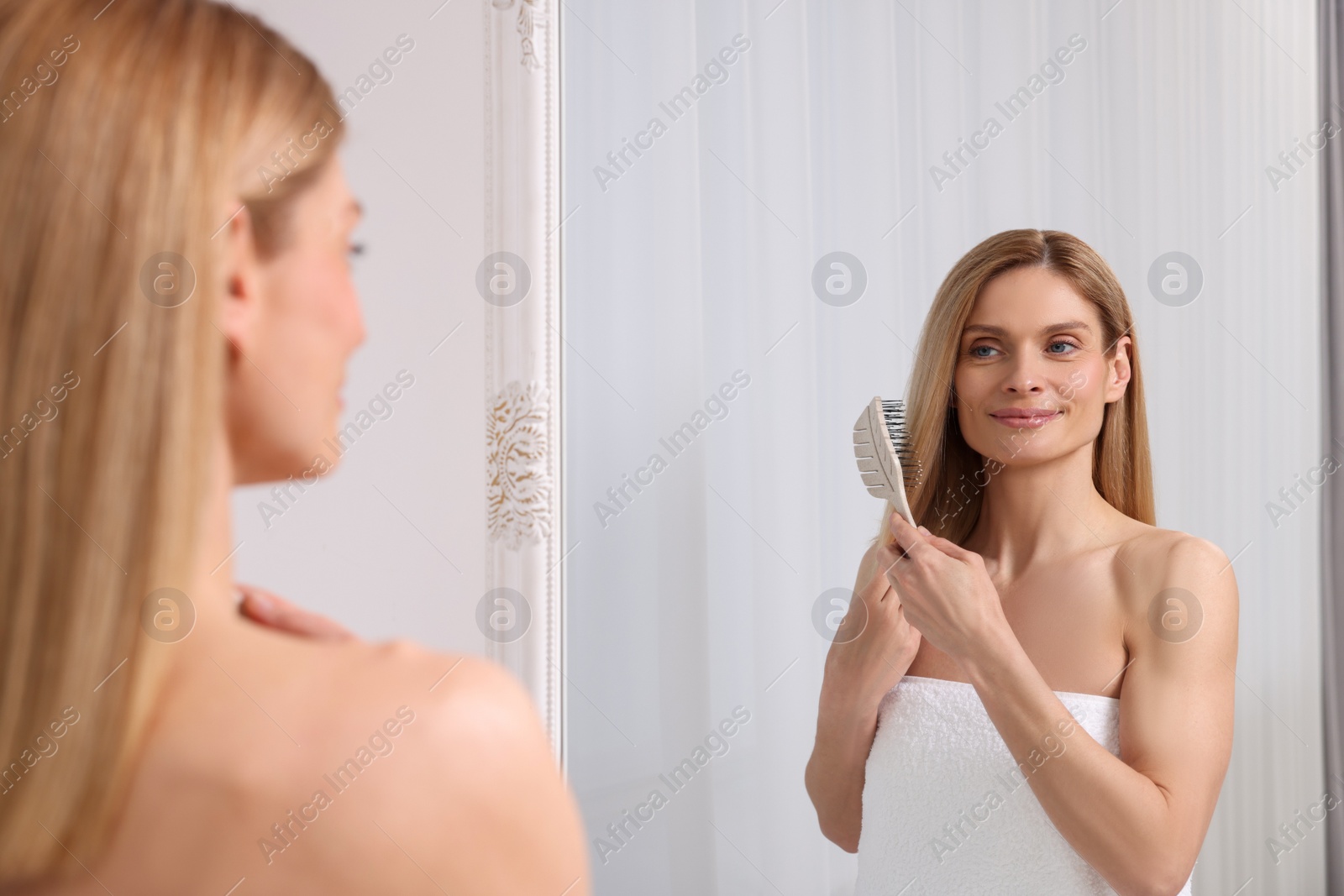 Photo of Beautiful woman brushing her hair near mirror in room