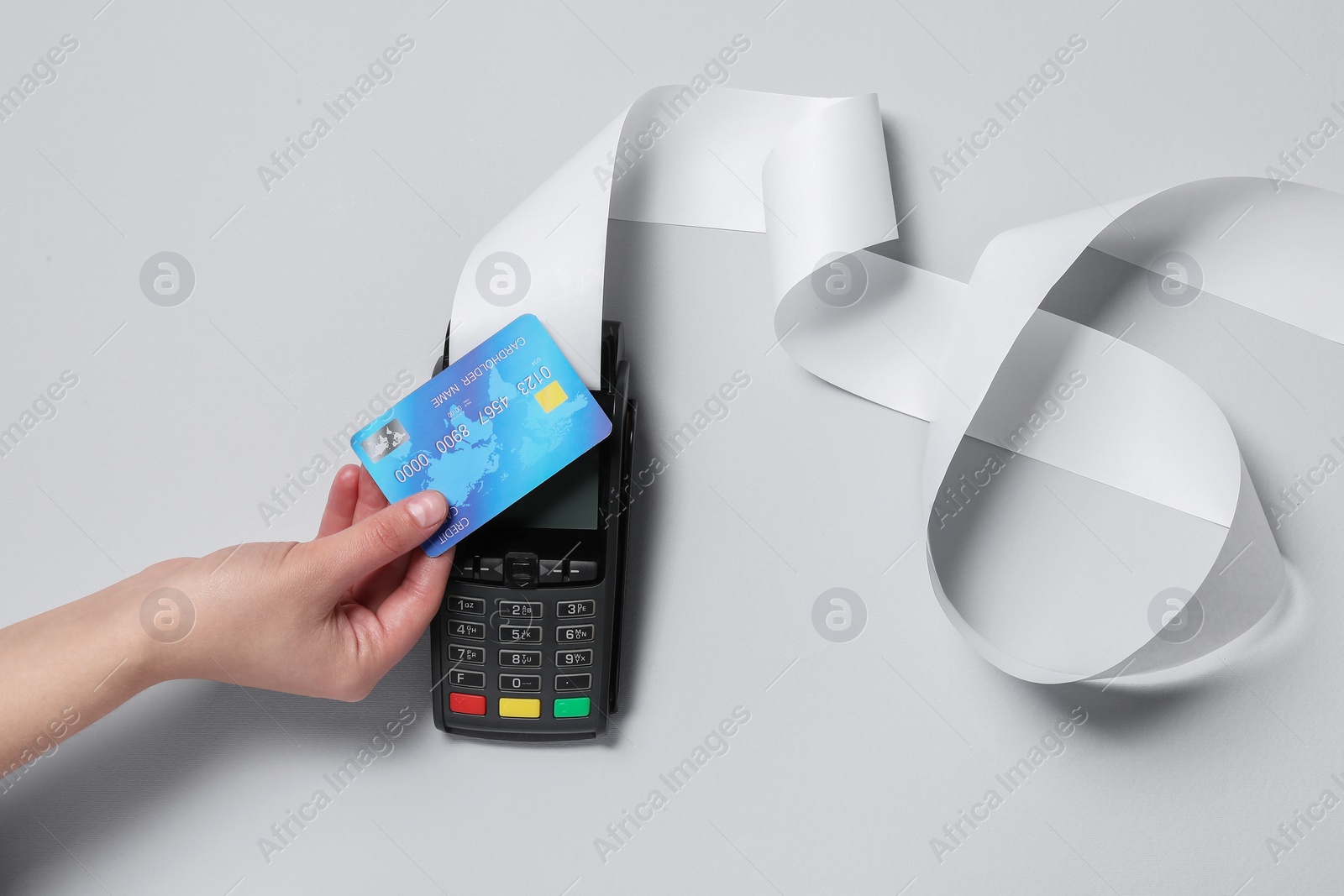 Photo of Woman using payment terminal with credit card and thermal paper for receipt on light grey background, top view