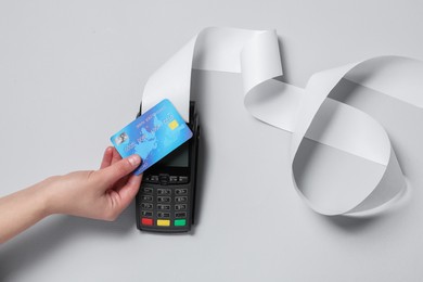 Photo of Woman using payment terminal with credit card and thermal paper for receipt on light grey background, top view