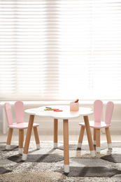 Photo of Little table and chairs with bunny ears near window in children's room. Interior design