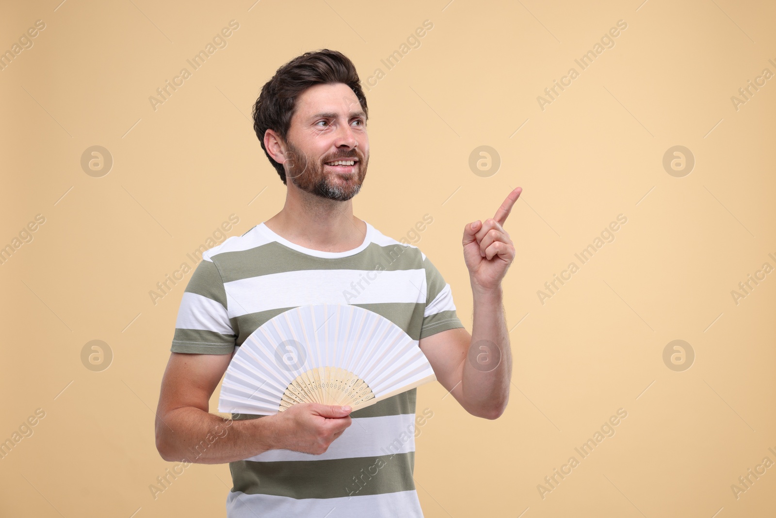 Photo of Happy man holding hand fan on beige background. Space for text