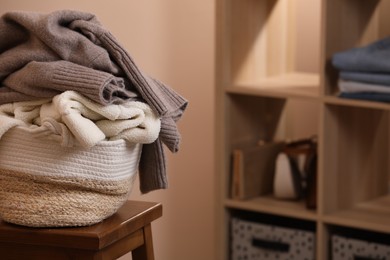 Photo of Wicker laundry basket overfilled with clothes on wooden stool indoors. Space for text