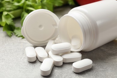 Photo of Dietary supplements. Overturned bottle and pills on grey textured table, closeup