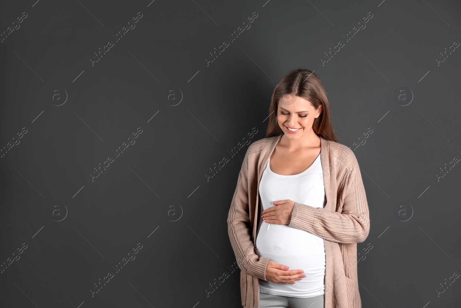 Photo of Young pregnant woman on grey background. Space for text