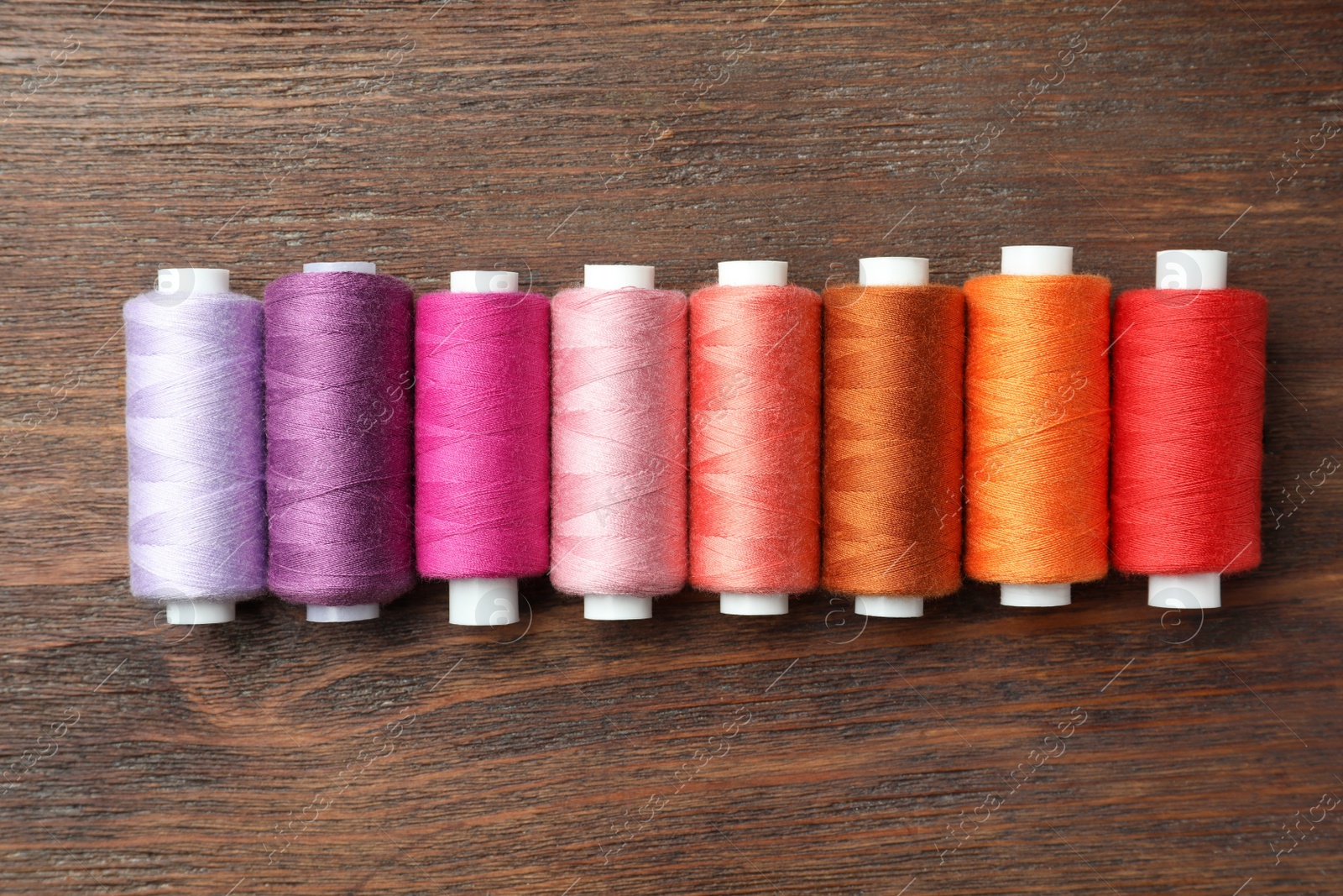 Photo of Set of colorful sewing threads on wooden table, flat lay