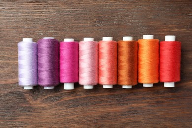 Set of colorful sewing threads on wooden table, flat lay