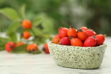 Ripe rose hip berries with green leaves on white wooden table outdoors, closeup. Space for text