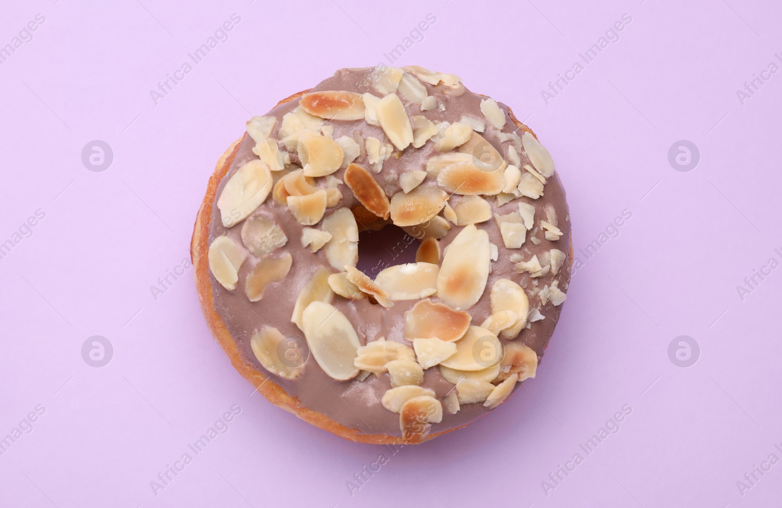 Photo of Tasty glazed donut decorated with nuts on purple background, top view