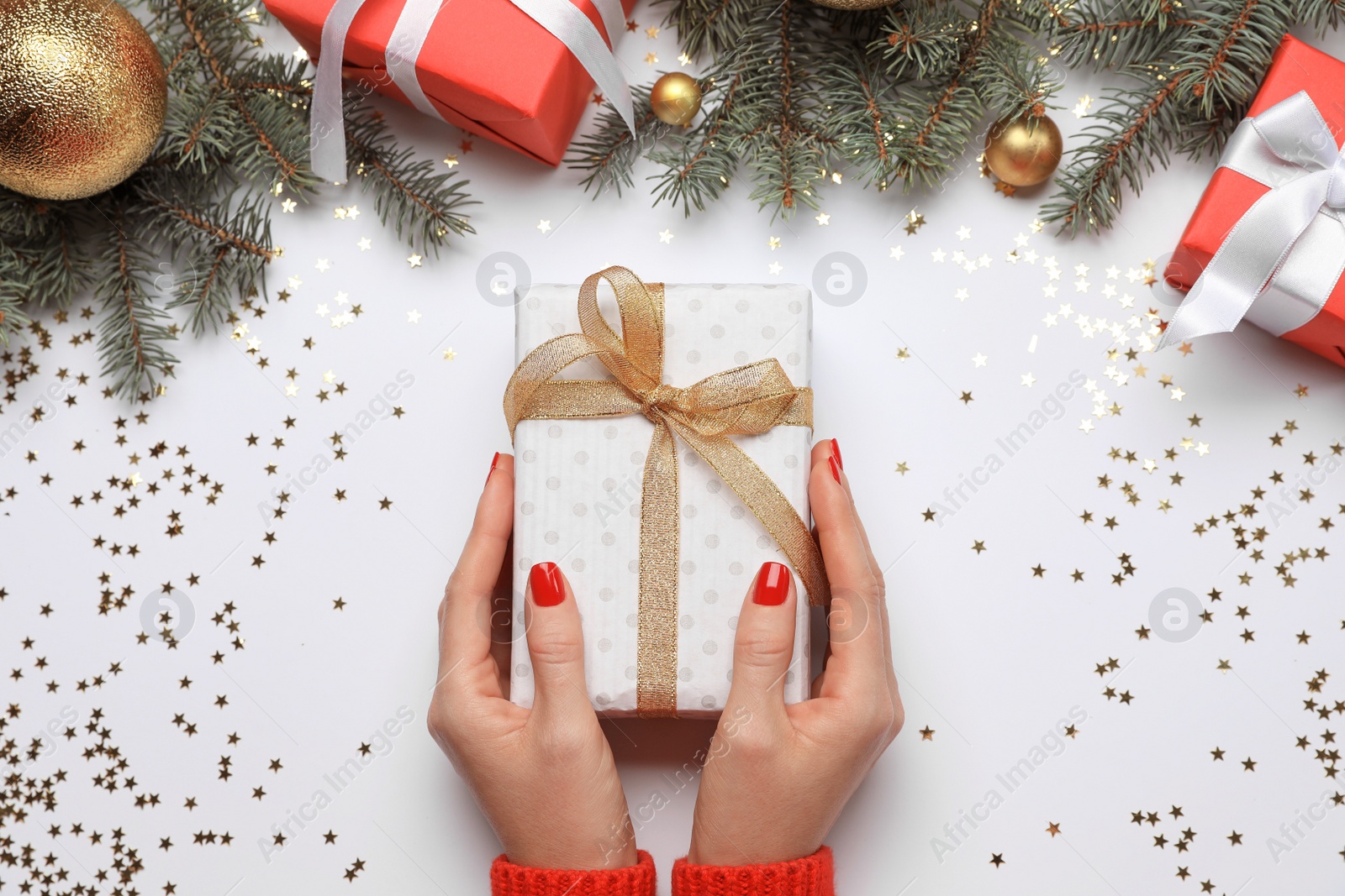 Photo of Woman holding gift box near fir tree branches with Christmas decor on white background, top view