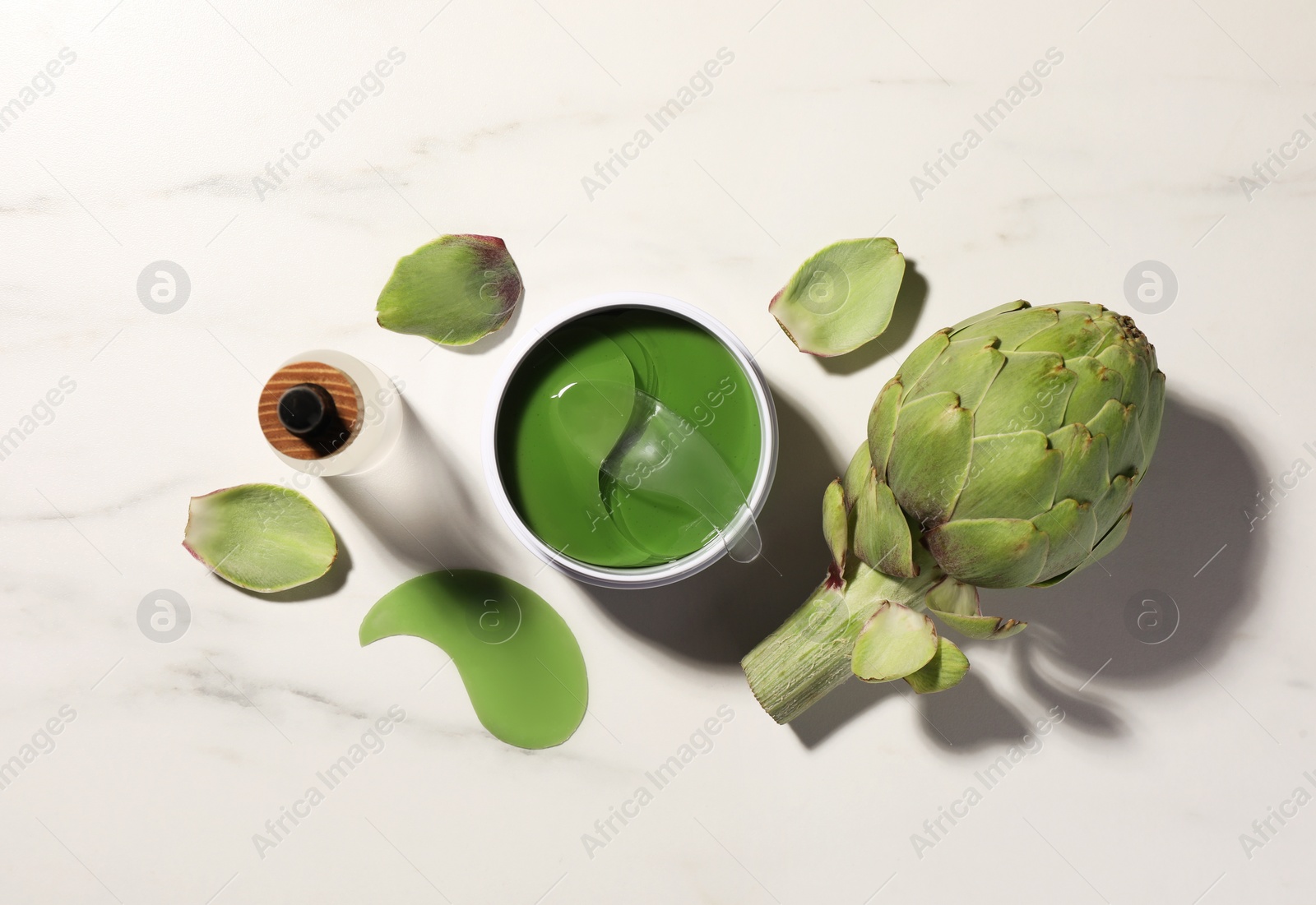 Photo of Package of under eye patches, cosmetic product and artichoke on white marble table, flat lay