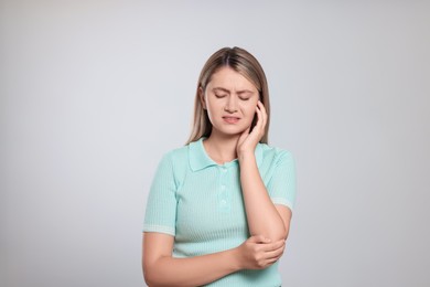 Young woman suffering from ear pain on light grey background