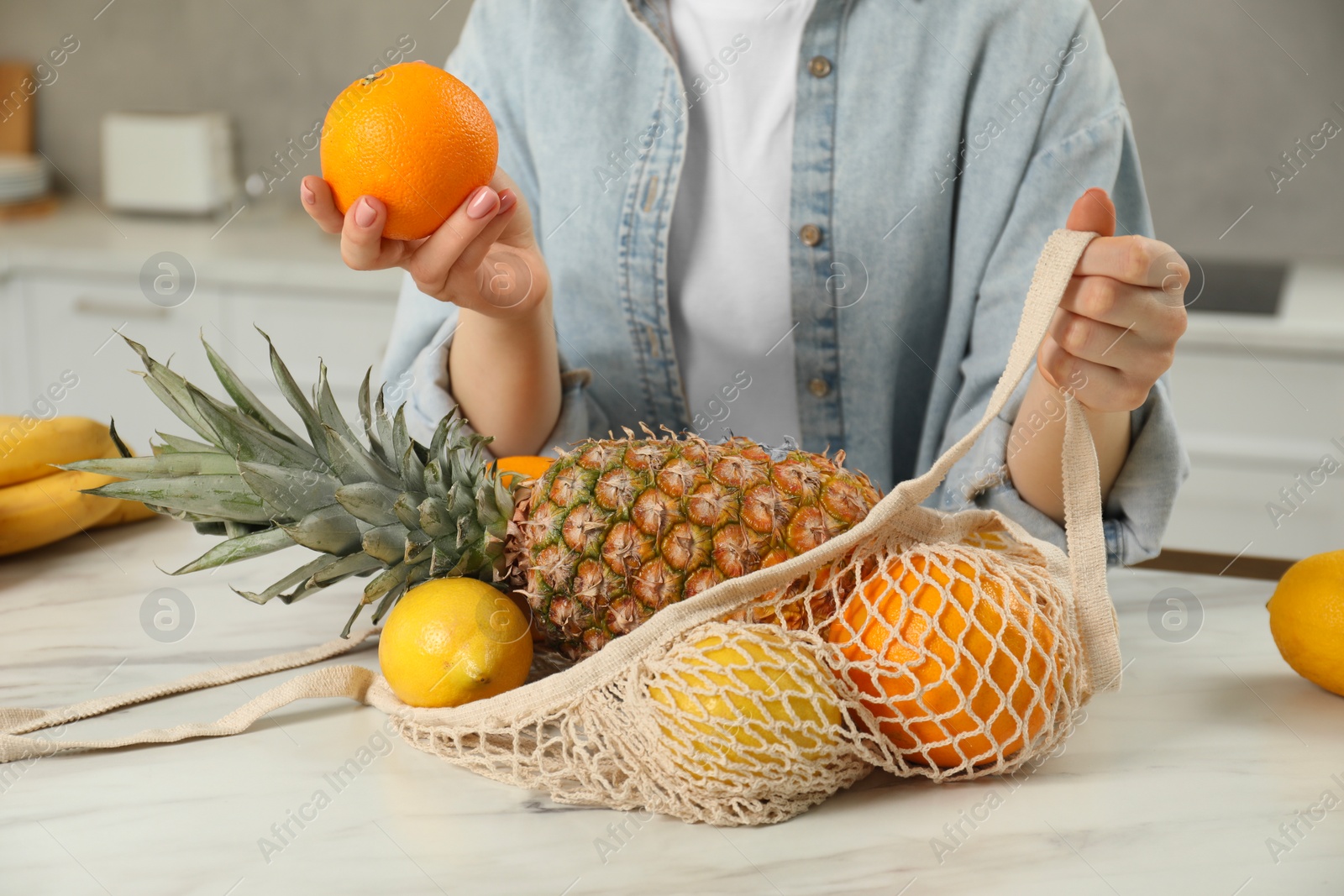 Photo of Woman with string bag of fresh fruits at light marble table, closeup