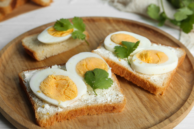 Photo of Tasty sandwiches with boiled eggs on wooden tray, closeup