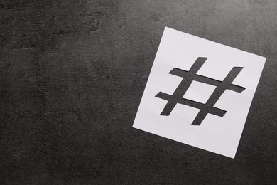 White paper stencil with symbol of hashtag on dark background, top view. Space for text