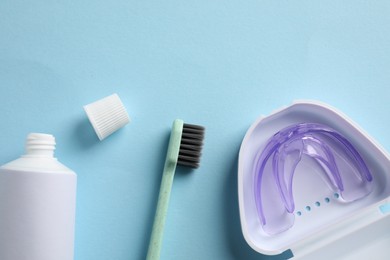 Bite correction. Toothpaste, brush and dental mouth guard on light blue background, flat lay. Space for text
