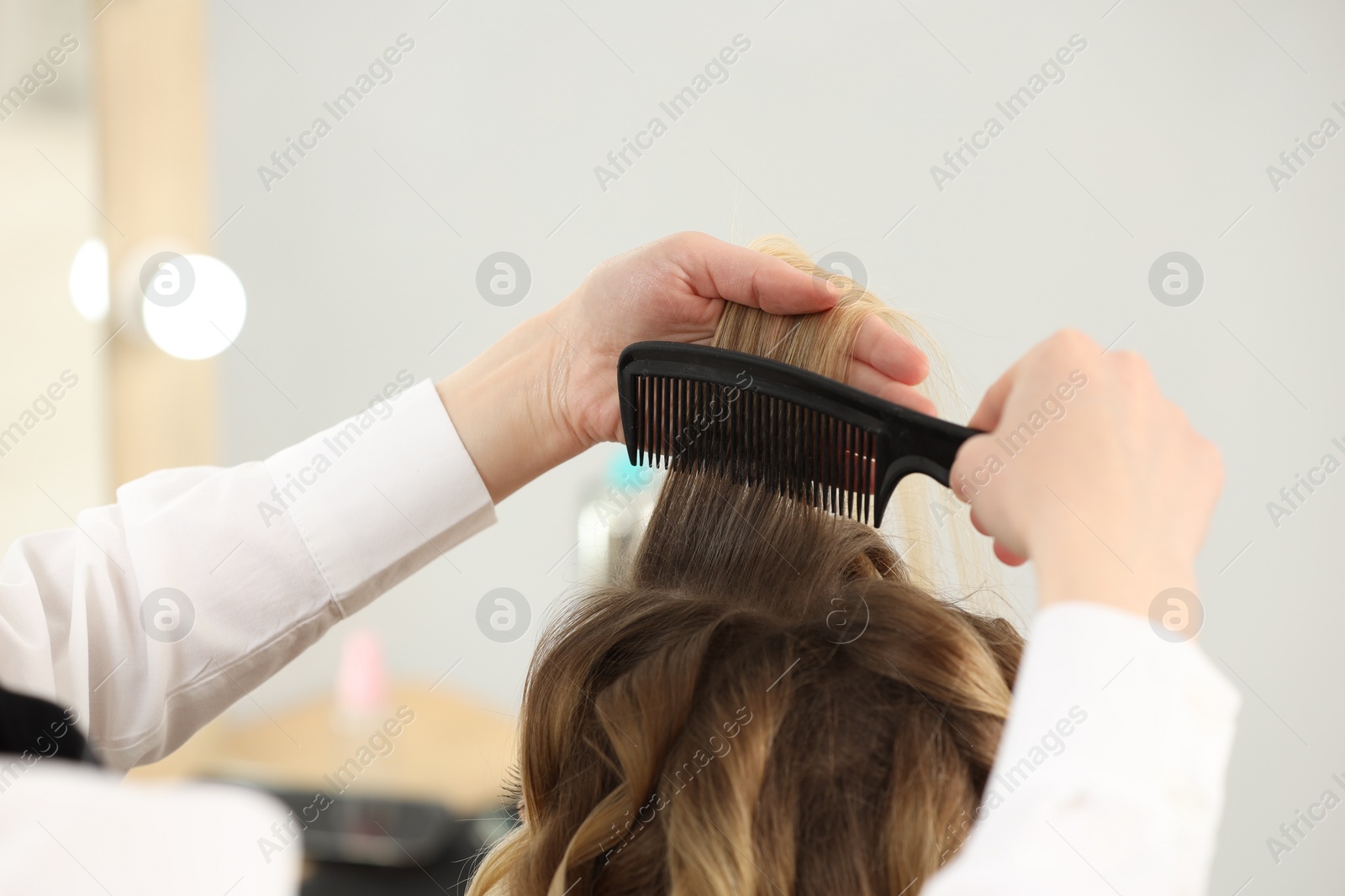 Photo of Hair styling. Hairdresser combing woman's hair indoors, closeup