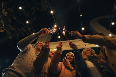 Group of people in warm clothes holding burning sparklers outdoors, low angle view