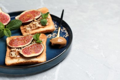 Photo of Tasty toasts served with fig, peanut butter and walnuts on white marble table. Space for text