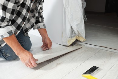 Photo of Professional worker installing new laminate flooring indoors, closeup
