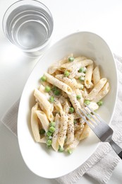 Delicious pasta with green peas, creamy sauce, water and fork on white table, top view