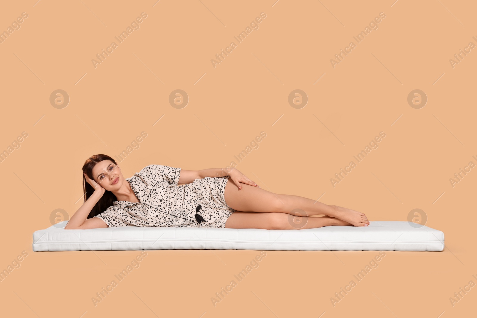 Photo of Young woman lying on soft mattress against beige background