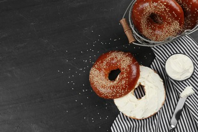 Photo of Delicious bagel with cream cheese on black table, flat lay. Space for text