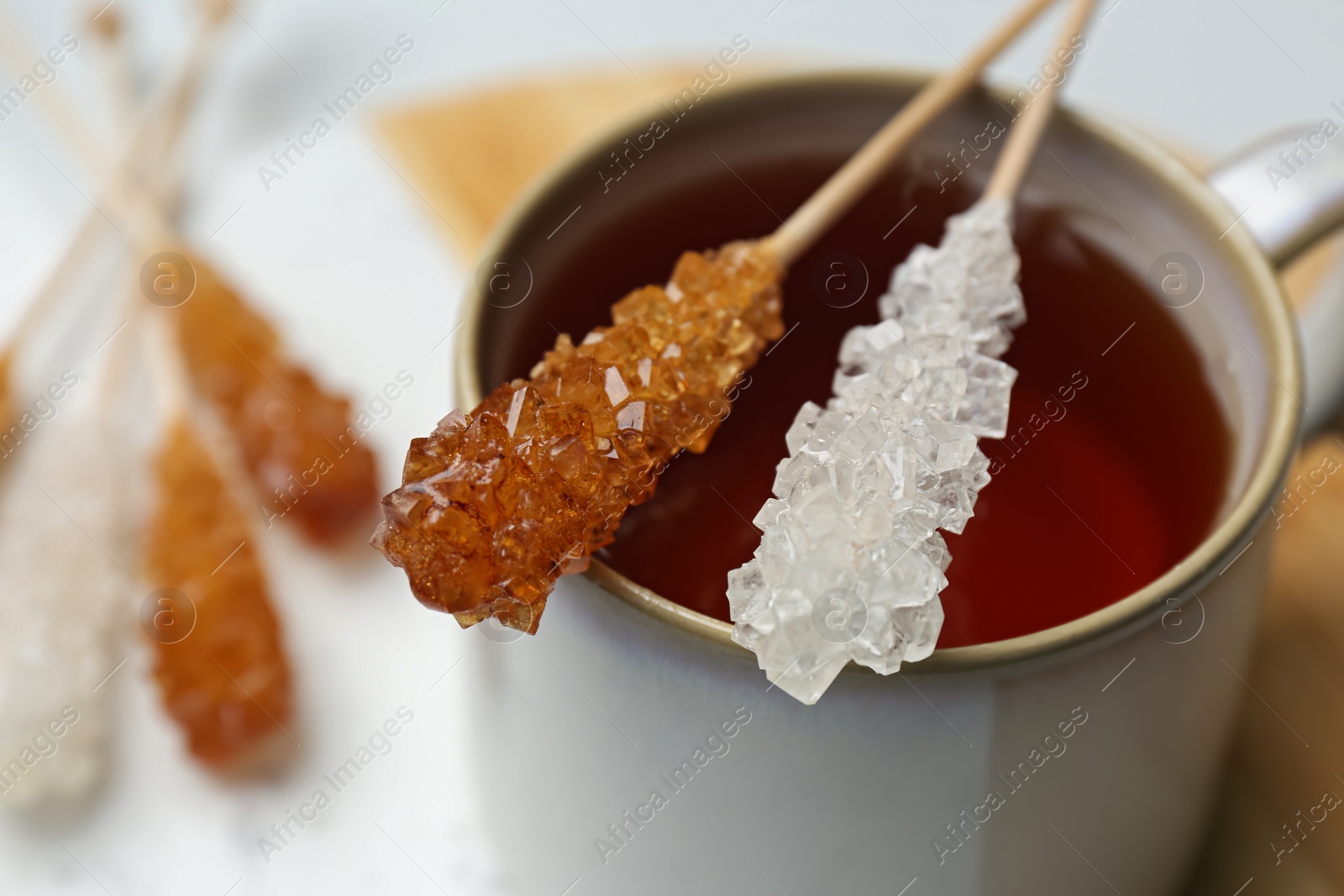 Photo of Sticks with sugar crystals and cup of tea on table, closeup