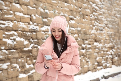 Photo of Young woman listening to music with headphones near stone wall