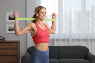 Athletic woman doing exercise with fitness elastic band at home. Space for text