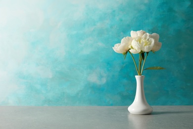 Photo of Fragrant peonies in vase on table against color background, space for text. Beautiful spring flowers