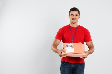 Happy young courier with parcel and envelopes on white background. Space for text