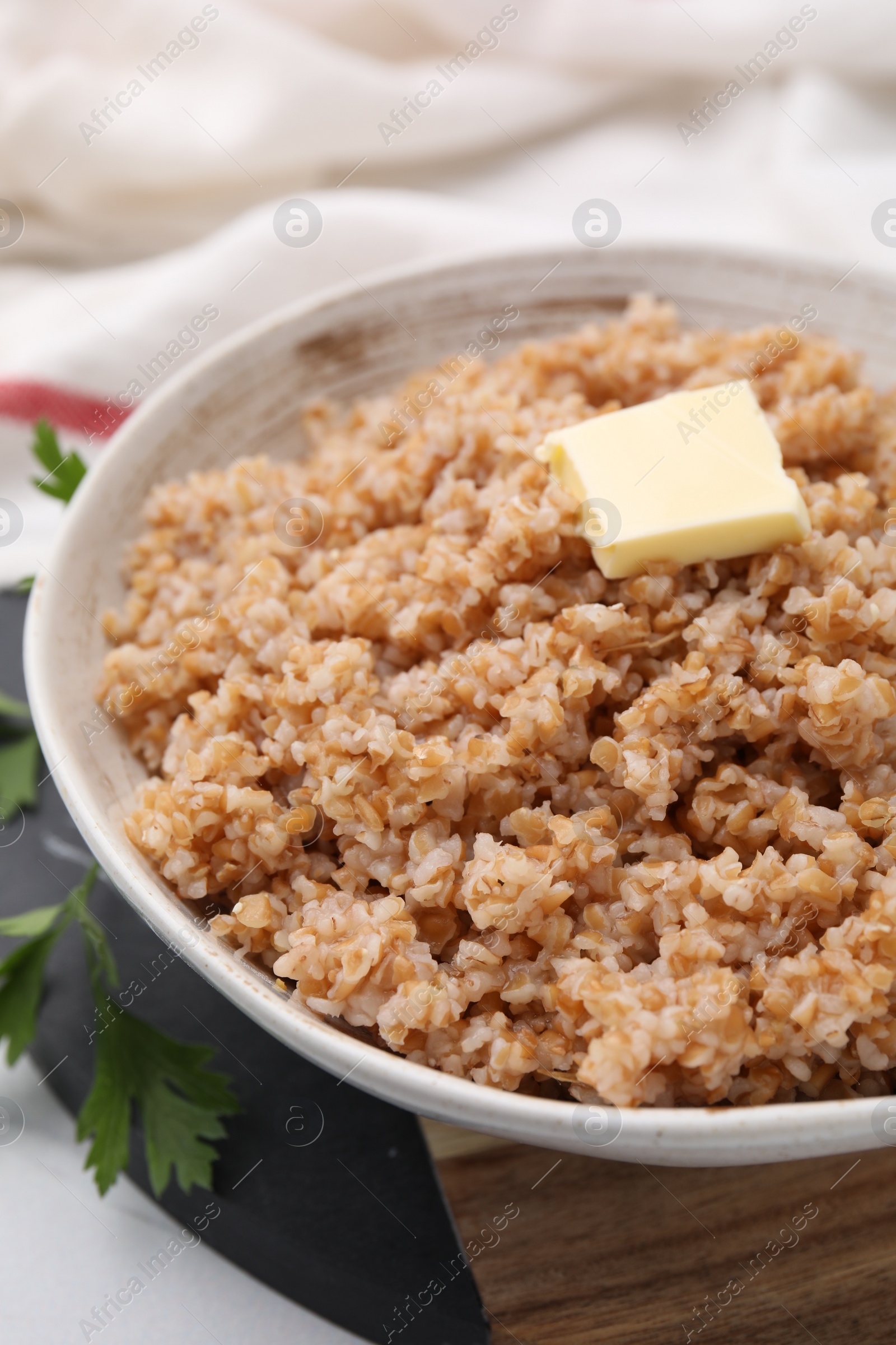 Photo of Tasty wheat porridge with butter and parsley in bowl on white table, closeup