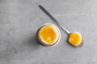 Fresh soft boiled egg in cup on grey table, flat lay