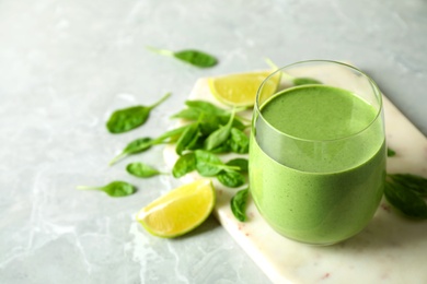 Glass of healthy green smoothie with fresh spinach on light table. Space for text