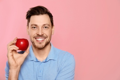 Photo of Smiling man with perfect teeth and red apple on color background. Space for text