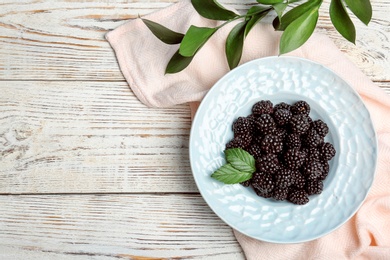 Photo of Flat lay composition with plate of fresh blackberry and space for text on wooden background