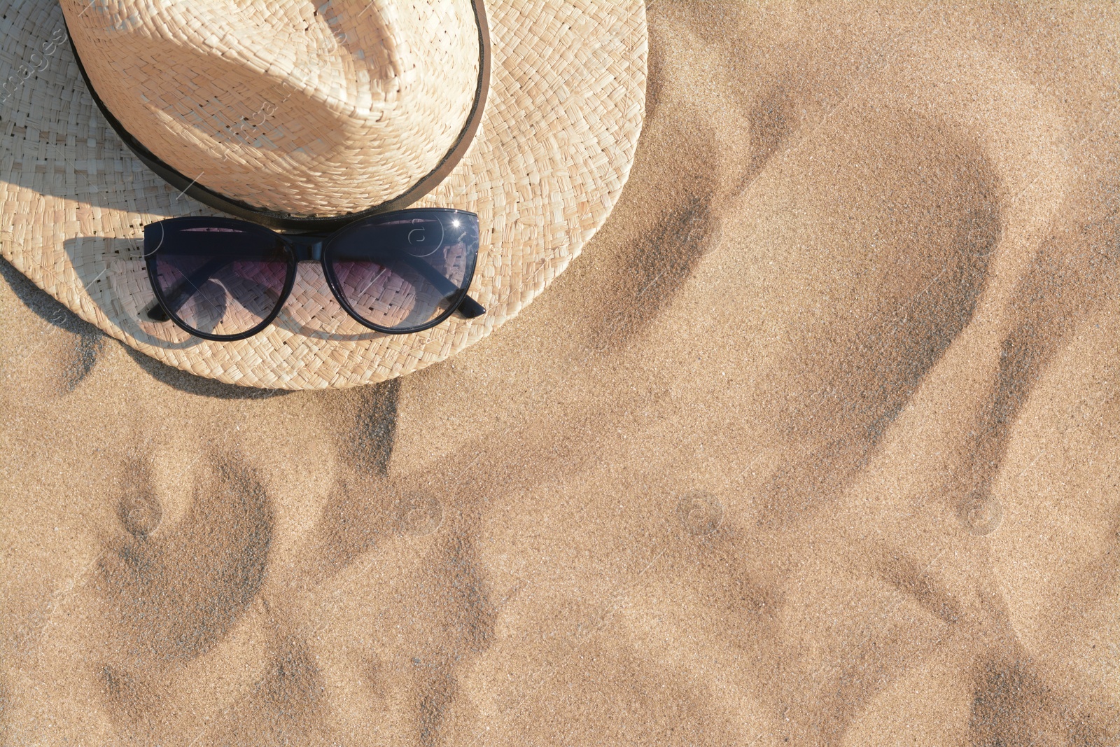 Photo of Hat with beautiful sunglasses on sand, top view. Space for text