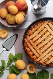 Delicious apricot pie in baking dish and fresh fruits on white wooden table, flat lay