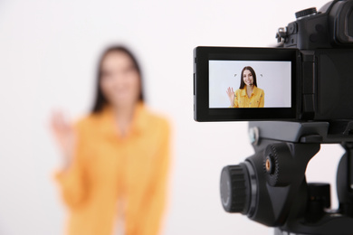 Photo of Young blogger recording video against white background, focus on camera screen