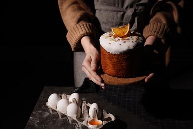 Photo of Young woman holding traditional decorated Easter cake on black background, closeup. Space for text