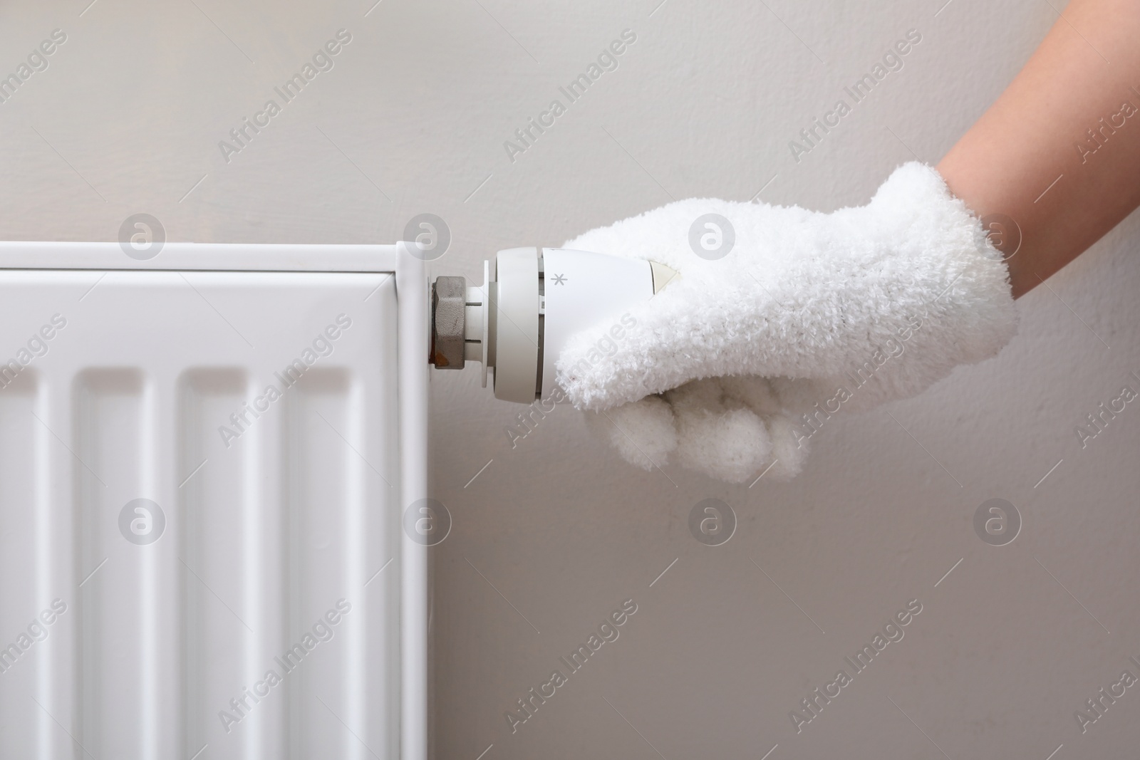 Photo of Girl in glove adjusting heating radiator thermostat near white wall, closeup