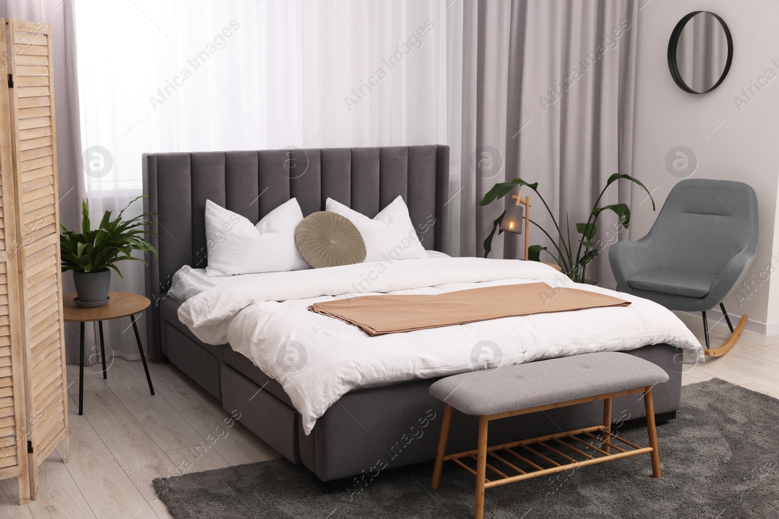 Photo of Stylish bedroom interior with large bed, ottoman, lamp and houseplants