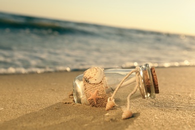 Photo of Wedding invitation in glass bottle on sandy beach at sunset