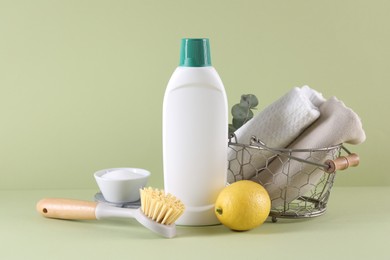 Bottle of cleaning product, baking soda, lemon and brush on light green background